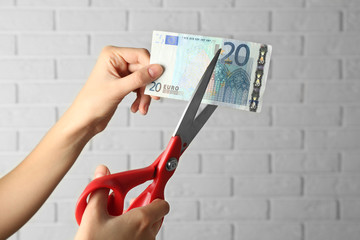 Hands with scissors cutting money on white brick wall background
