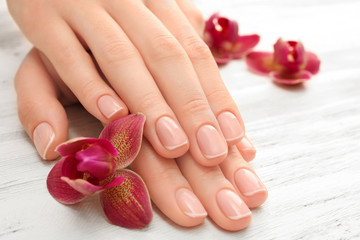 Woman hands with beautiful manicure and purple orchid on wooden background, close up