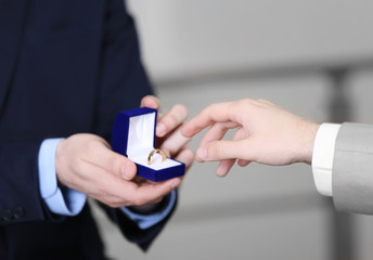One groom is going to put wedding ring on another man's finger on blurred background