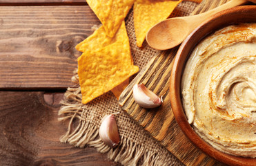 Wooden bowl of tasty hummus with chips on table