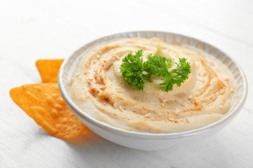 Ceramic bowl of tasty hummus with chips and parsley on table