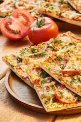 Pieces of pizza with ham and cheese sprinkled with herbs with tomato lie on a wooden table