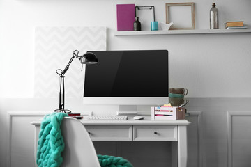 Modern wide screen monitor with lamp on white table in room interior