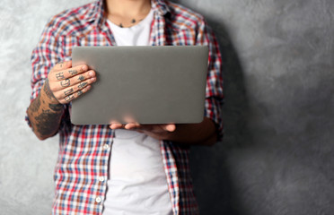 Young man with tattoo holding laptop on grey background