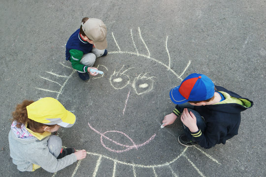Children is drawing sun on asphalt in spring park.