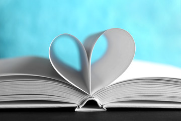Sheets of book curved into heart shape on unfocused blue background