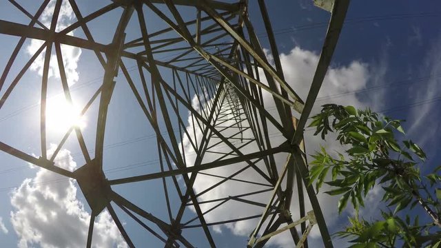 Electrical pylon from beneath against blue cloudy sky on sunny windy day, time lapse 4K

