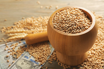 Dollar banknotes and wheat grains in bowl on wooden background. Agricultural income concept