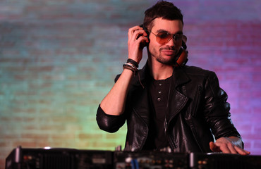 DJ playing music at mixer on blurred brick wall background