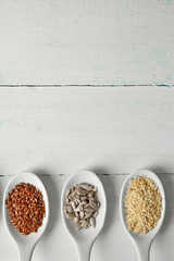 Different kinds of seeds in spoons on wooden table