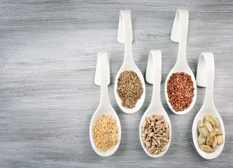 Different kinds of seeds in spoons on wooden table