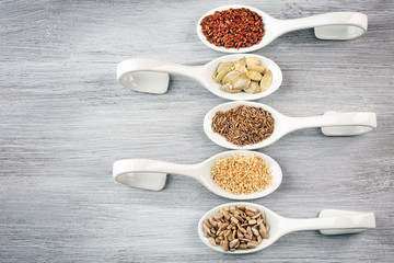 Different kinds of seeds in spoons on wooden table