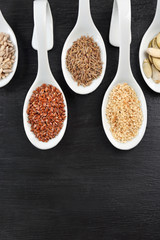 Different kinds of seeds in spoons on wooden table