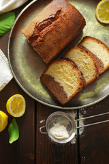 Delicious sweet cake bread in metal tray with lemons on wooden table, top view