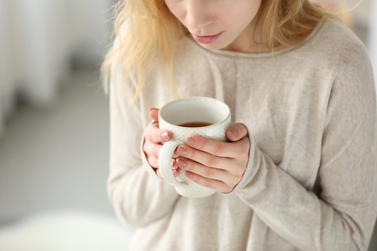 Woman in a white knitted sweater holding a cup of tea in her hands, close up