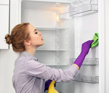Young woman cleaning empty fridge with a sponge