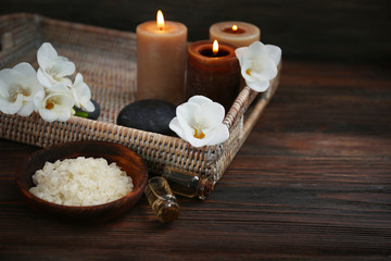 Fototapeta na wymiar Spa set with sea salt, exotic flowers and candles on wicker tray