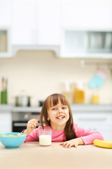 Beautiful little girl having breakfast with cereal, milk and banana in kitchen