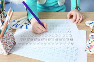 Little girl learning to write English letters at the table