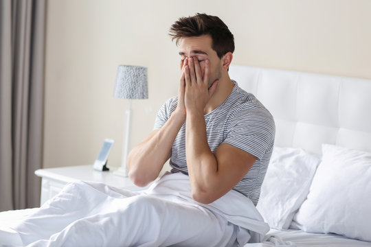 Sleepy Young Man Rubbing His Eye In Bed At Home