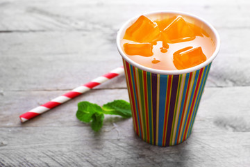 Orange drink in bright paper cup on wooden background © Africa Studio
