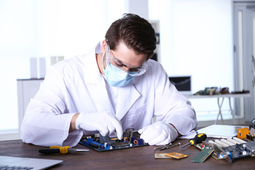 Man in white coat repairing electronic circuits in service center