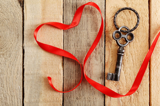 Old key and red ribbon on wooden background