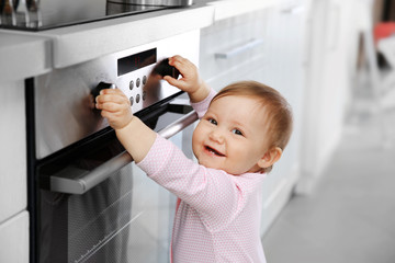 Little child playing with electric stove in the kitchen - obrazy, fototapety, plakaty