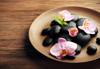 Spa stones and orchid flowers in plate on wooden background
