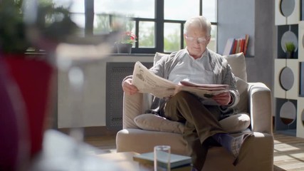 elderly man sits in a chair and reading a newspaper in a modern apartment - Powered by Adobe