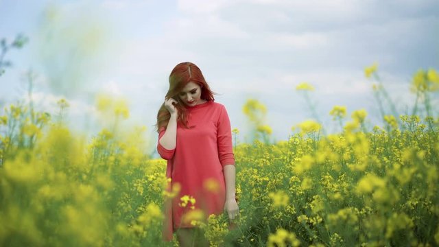 Girl with bouquet of rape blossom in the field, wind blowing, cloudy sky 4k