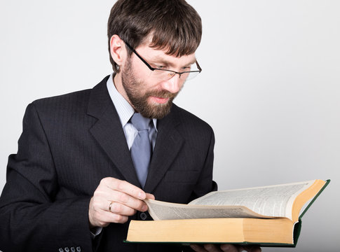 bearded businessman in a business suit and tie, reading a thick book
