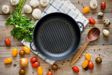

Cooking ingredients for a healthy and vegan life: cherry tomatoes, onion, mushrooms, spices and greens on rustic wooden backdrop. Empty skillet in middle. Top view, copy space for text