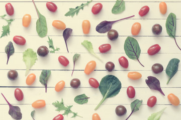 Naklejka na ściany i meble Cherry tomatoes and green salad leaves on white wooden background. Top view, flat lay food. Vintage toning