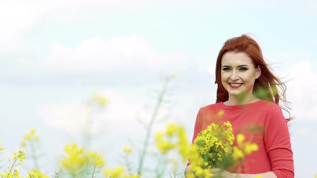 Girl with golden hair with bouquet of rape bloom smiling in the field. Slowly