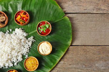 Boiled rice with vegetables and spices on banana leaf over wooden background