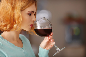 Young woman with glass of red wine on light blurred background
