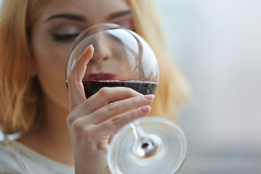 Young woman with glass of red wine on light blurred background