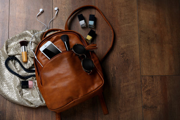 Brown leather backpack with female items on wooden surface, top view