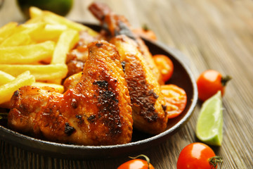 Baked chicken wings with French fries on wooden table