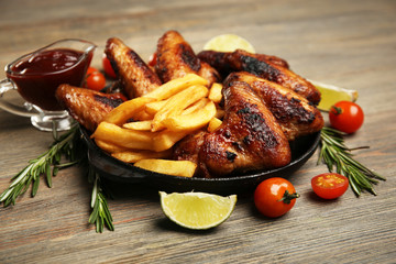Baked chicken wings with French fries on wooden table