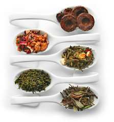 Different sorts of dry tea in ceramic spoons, isolated on white