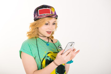 Portrait of young girl with a phone. Trendy Casual Fashion Outfit in Spring. Beautiful girl in a bright youth clothing, gay t-shirt, cap and suspenders for jeans. 

