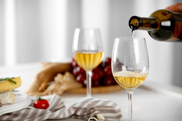 Pouring white wine into glass and food on table indoors