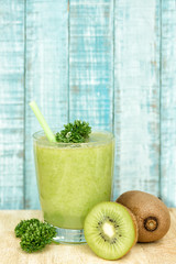 Green kiwi smoothie decorated with celery on wooden background