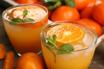 Delicious tangerine cocktails with ice, mint on a wooden table, close up