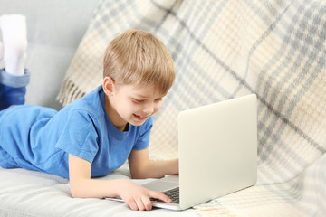 Little boy using laptop on sofa indoors