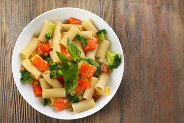 Plate of pasta with salmon and broccoli on wooden table, top view