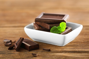 Chocolate with mint in a white bowl on wooden table.