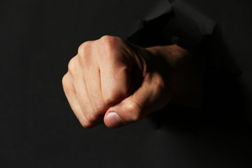 Male fist punching through black paper